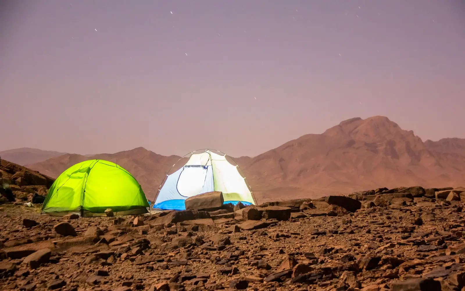 Dos casas de campaña tipo domo sobre terreno rocoso rojizo del desierto al atardecer
