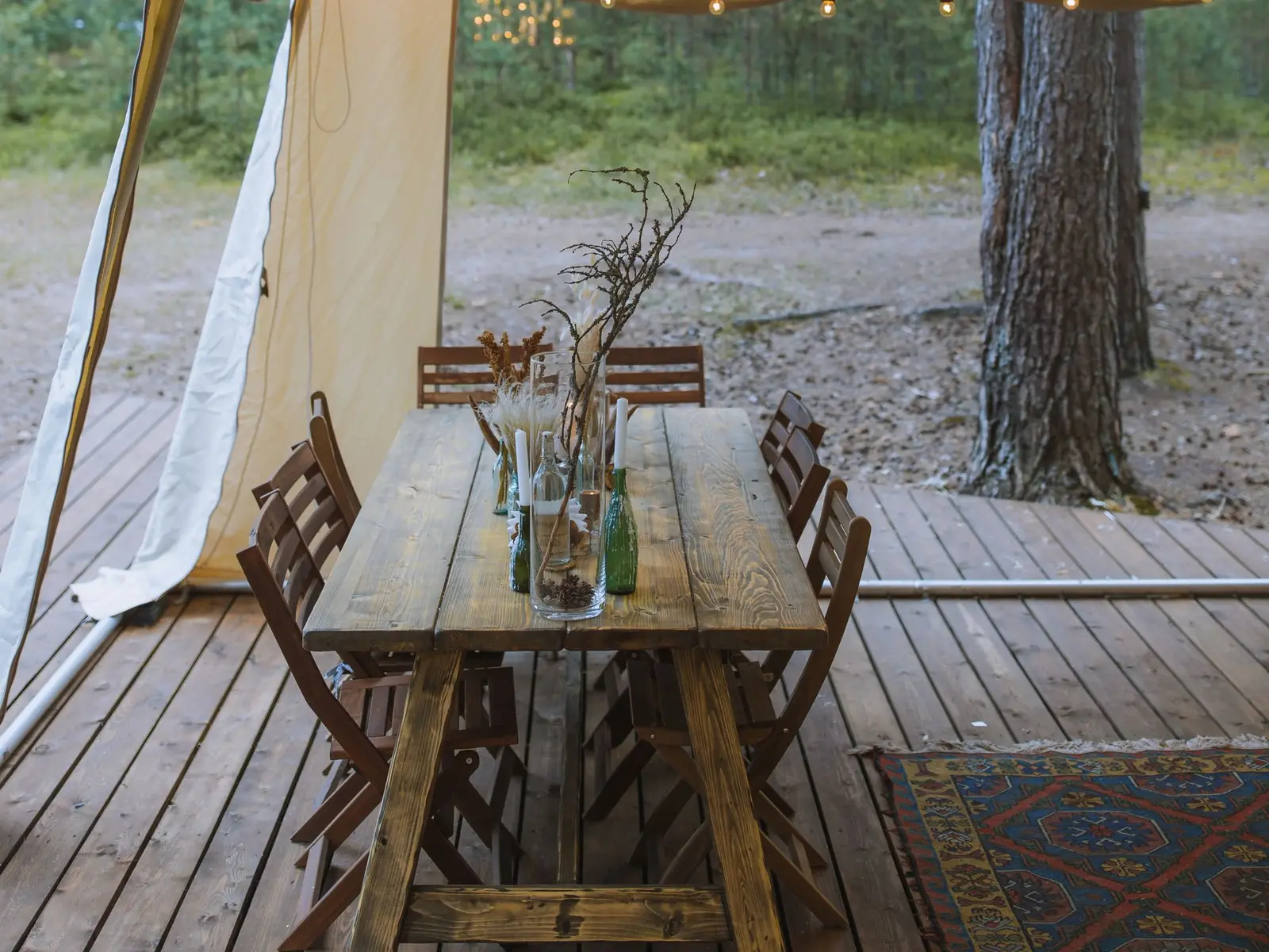 Terraza de madera de una tienda de glamping con mesa rústica, sillas y vista al bosque