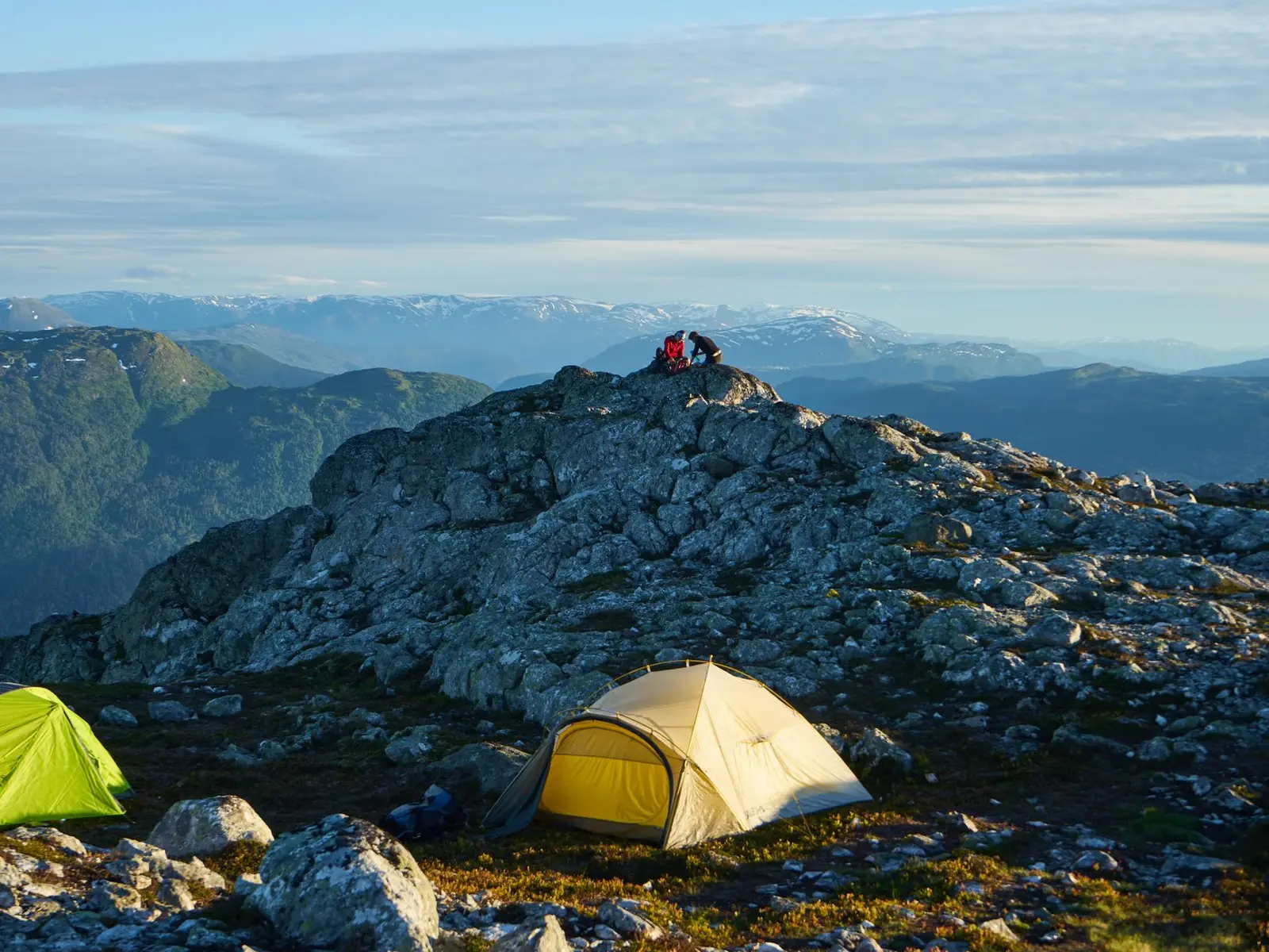 Casas de campaña amarilla y verde sobre una cima rocosa con vista a cordilleras al amanecer